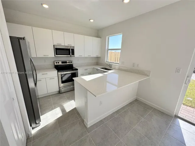 a white kitchen with a sink a microwave a refrigerator and cabinets