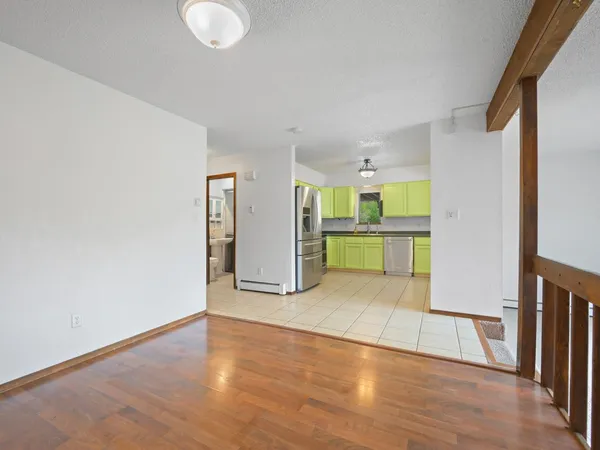 a view of an empty room with wooden floor and a kitchen