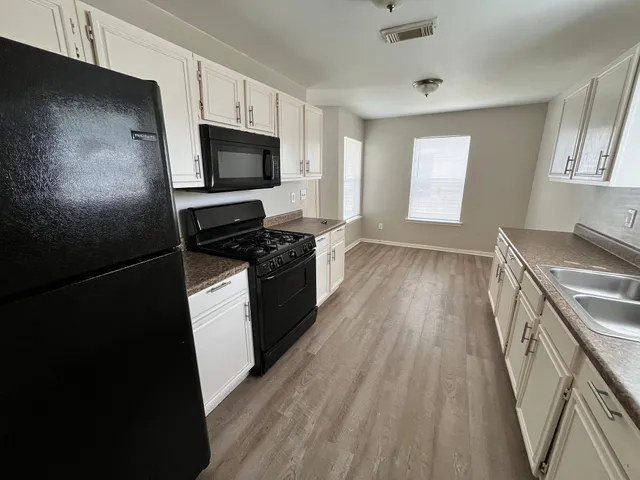 a kitchen with granite countertop a stove top oven a sink and white cabinets with wooden floor