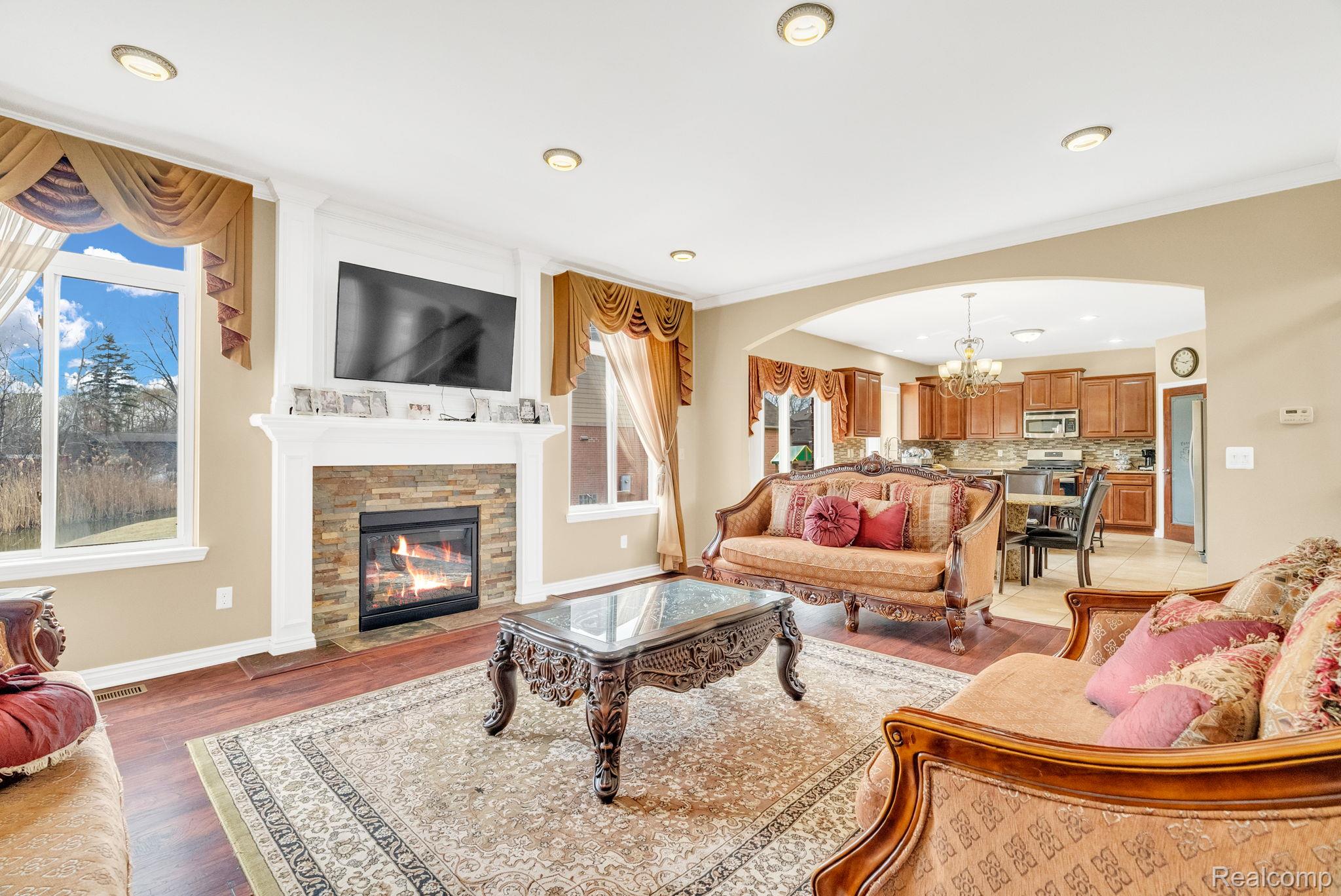 4122 Hawks Nest Road Utica, MI 48317 - Photo 20 of 74 Living room with arched walkways, a fireplace with flush hearth, a chandelier, light wood-type flooring, and crown molding