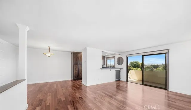 a view of empty room with wooden floor and kitchen