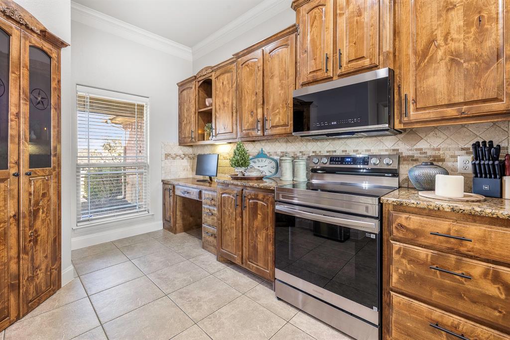 116 Miramar Circle Weatherford, TX 76085 - Photo 4 of 37 Entrance to kitchen from entry, features beautiful wood-stained cabinets, a desk, wooden surround on pantry, and new stainless steel appliances (2025), crown molding, granite counters, open shelves, and light ceramic tile floors