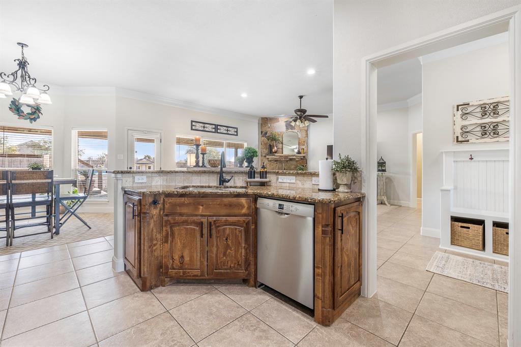 116 Miramar Circle Weatherford, TX 76085 - Photo 6 of 37 Kitchen sink overlooks living and dining areas; wood-stained cabinets with additional side storage, crown molding, Bosch dishwasher (2024), granite countertops, and hanging light fixtures. Lots of windows for natural light and view of pool and outdoor living area