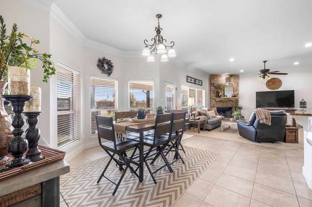 116 Miramar Circle Weatherford, TX 76085 - Photo 8 of 37 Open concept dining space that is connected to living room and kitchen. Dining room features ceramic tile and has room for a coffee bar; large windows let in tons of natural light and also has a chandelier. Living room features additional windows for even more light, carpet, a stone wood-burning fireplace and a ceiling fan and ornamental molding detail.