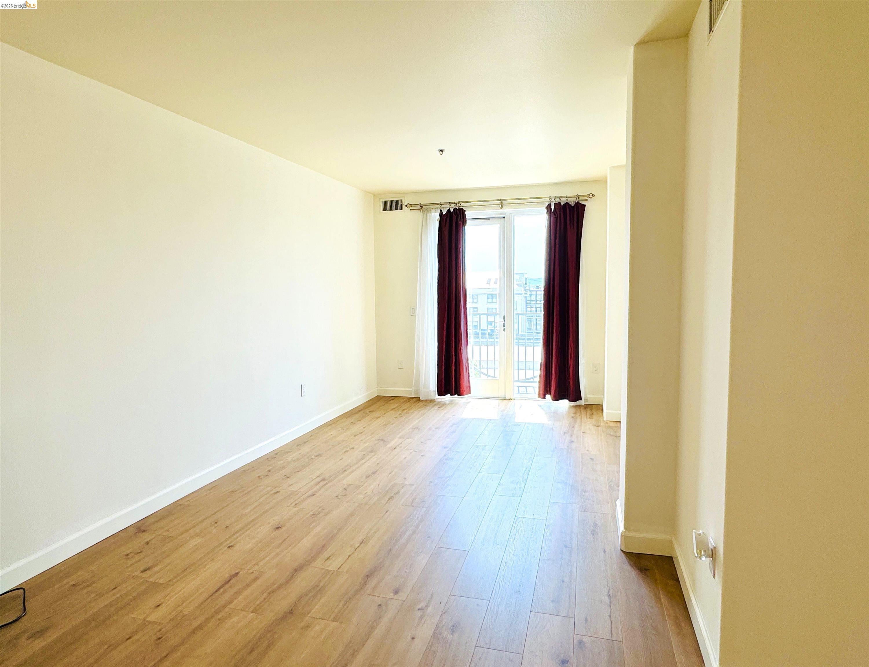 423 7th Street, Unit 303 Oakland, CA 94607 - Photo 18 of 19 an empty room with wooden floor and windows with curtains