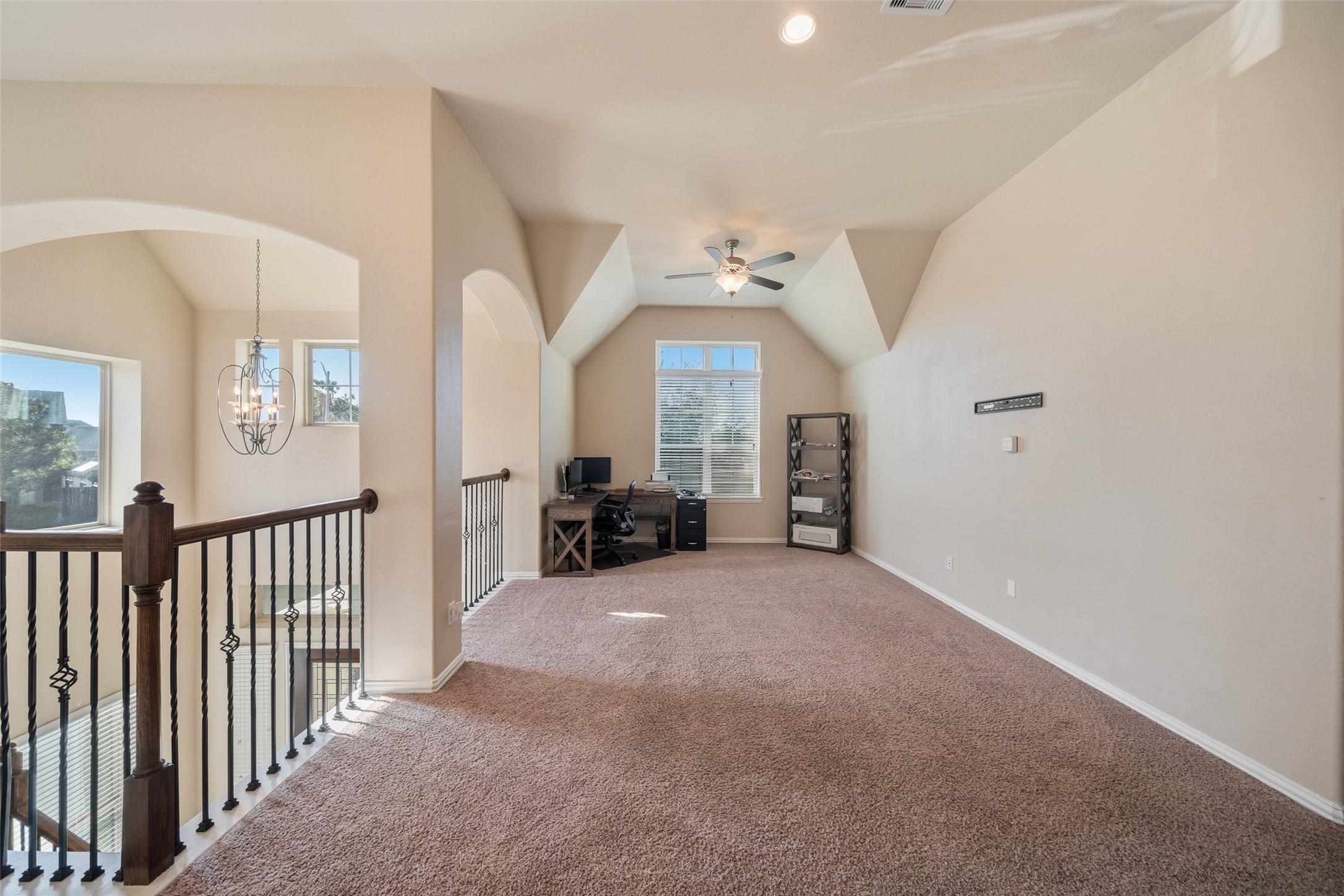 4747 Abercorn Street Rosharon, TX 77583 - Photo 23 of 46 This spacious loft features a cozy carpeted area with a ceiling fan and ample natural light from large windows. An open railing overlooks the floor below, and a chandelier adds elegance. It’s ideal for a home office or relaxation space.