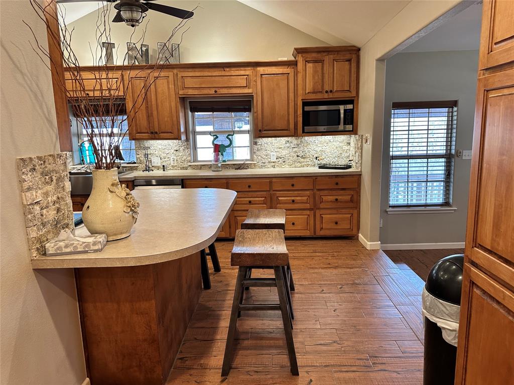 11001 West Lake Road Abilene, TX 79601 - Photo 24 of 40 Kitchen featuring brown cabinets, vaulted ceiling, decorative backsplash, and stainless steel microwave