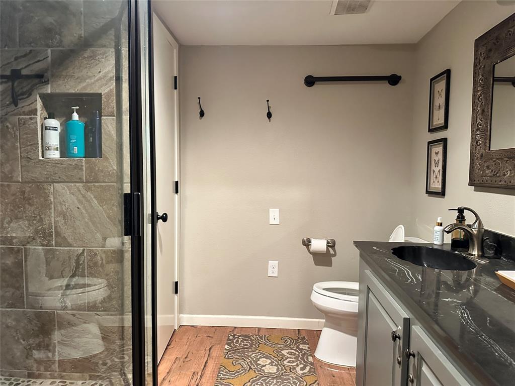 11001 West Lake Road Abilene, TX 79601 - Photo 25 of 40 Full bath featuring toilet, vanity, a shower stall, wood finished floors, and baseboards