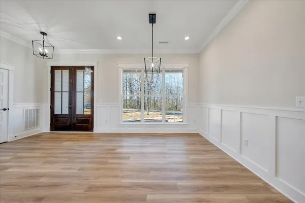 an empty room with wooden floor kitchen view and a chandelier