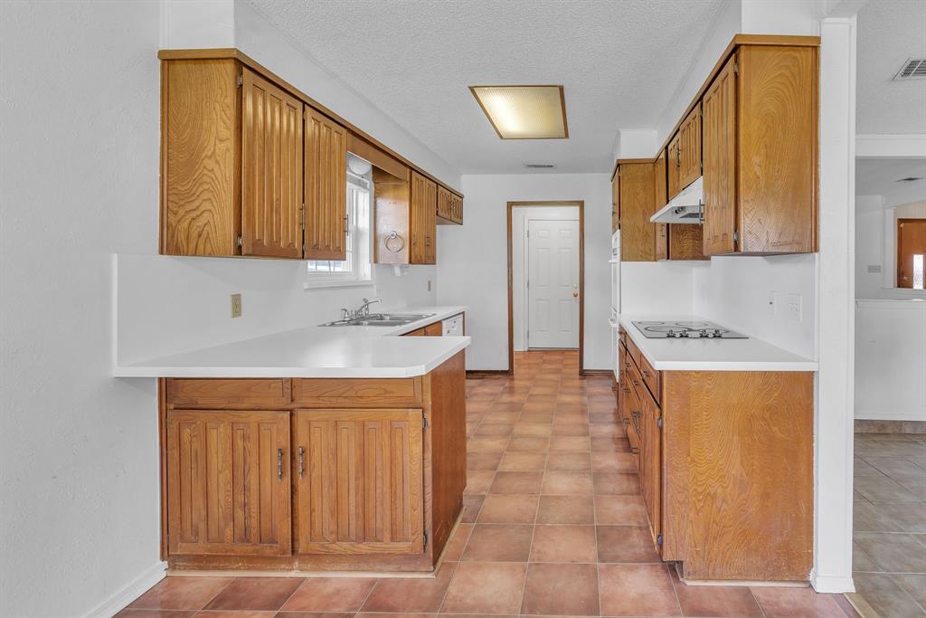 1720 Timbercreek Road Benbrook, TX 76126 - Photo 8 of 33 Galley kitchen featuring wood-finish cabinetry, white countertops, a built-in cooktop, and tile flooring