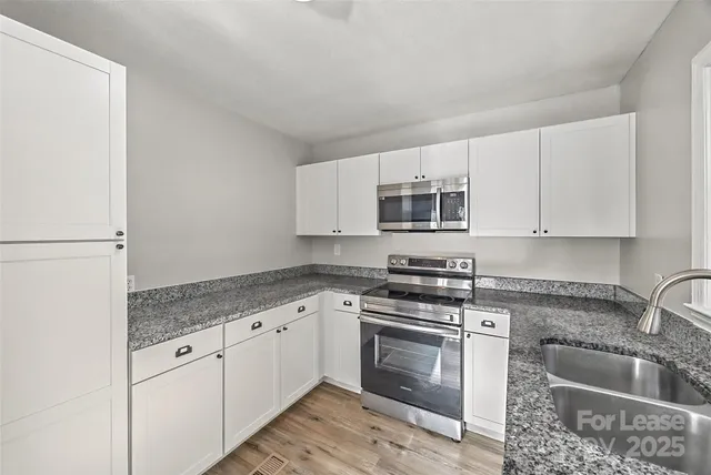 a kitchen with granite countertop white cabinets sink and stainless steel appliances