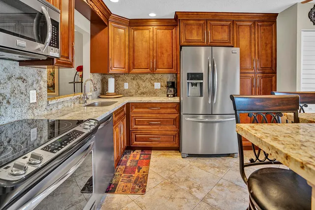 a kitchen with stainless steel appliances granite countertop a refrigerator a stove and a sink with wooden cabinets