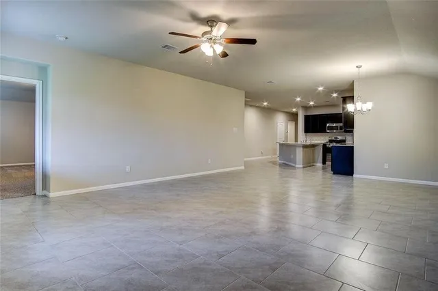 an empty room with a kitchen and a chandelier fan