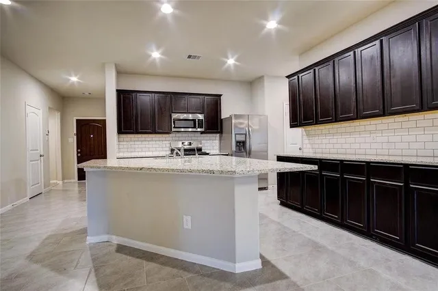 a kitchen with stainless steel appliances kitchen island granite countertop a stove a sink dishwasher and a microwave oven with wooden cabinets