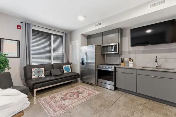 a living room with stainless steel appliances furniture a flat screen tv and a window