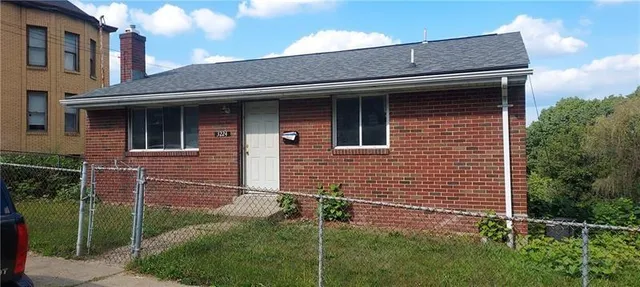 a brick house that has a small yard and large trees