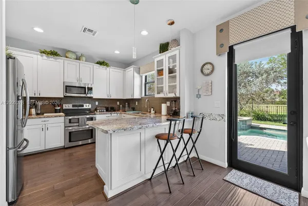 a kitchen with kitchen island granite countertop a stove a sink a refrigerator and white cabinets with wooden floor