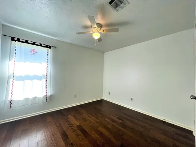 an empty room with wooden floor fan and windows
