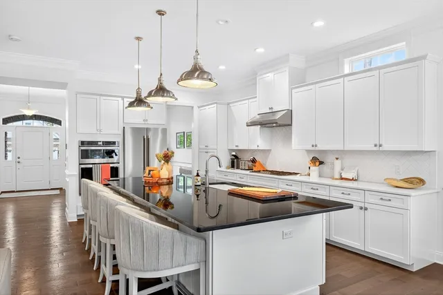 a kitchen with stainless steel appliances granite countertop a sink a stove a refrigerator cabinets and chairs