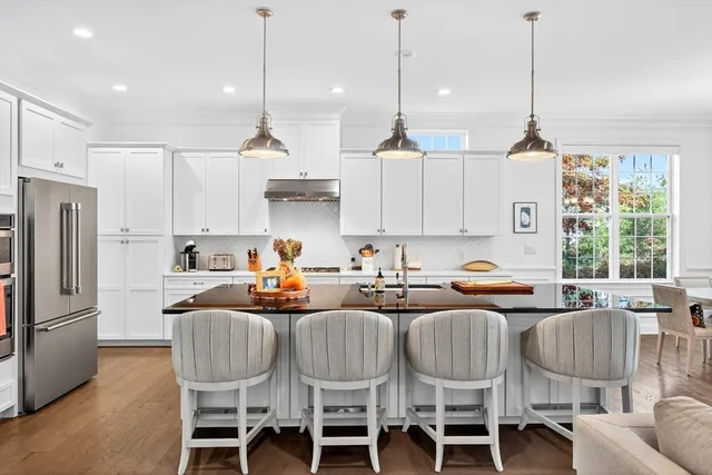 a kitchen with stainless steel appliances granite countertop a refrigerator a stove a kitchen island a dining table and chairs