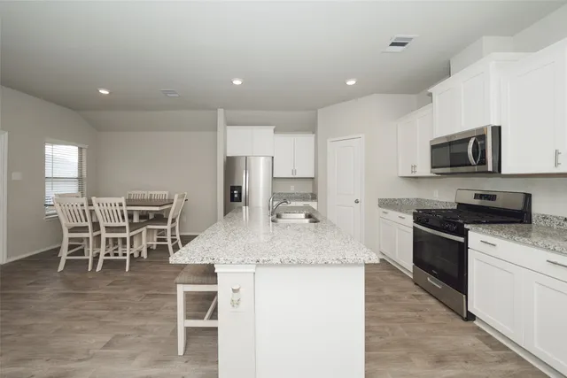 a kitchen with stainless steel appliances granite countertop a stove top oven a sink a dining table and chairs