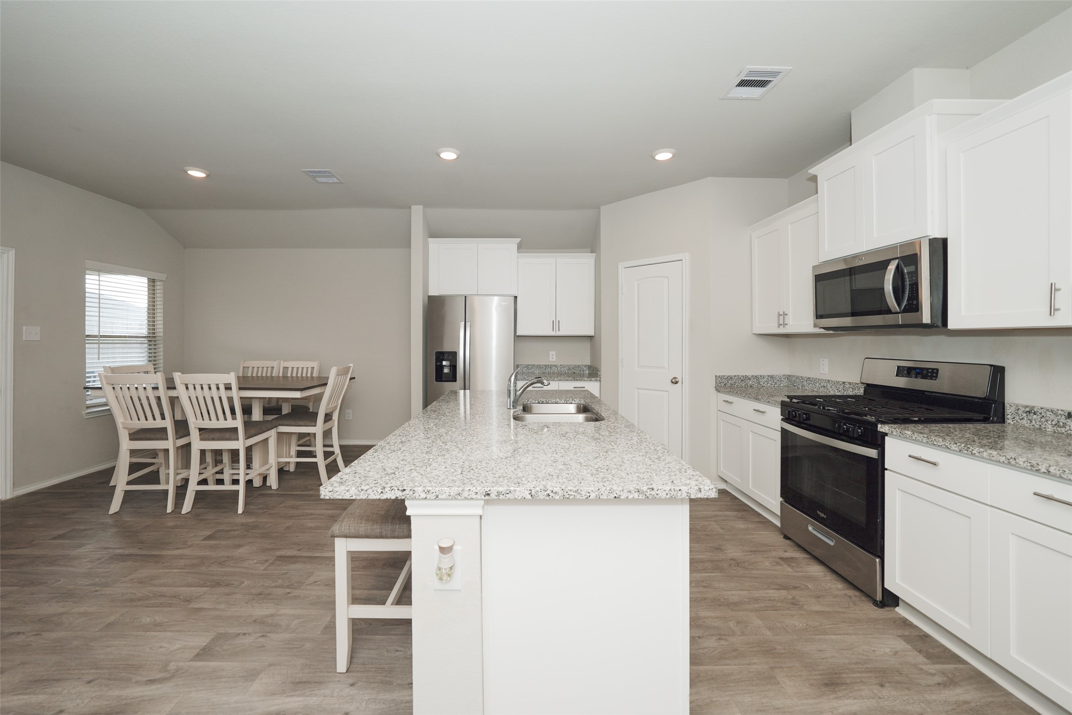 a kitchen with stainless steel appliances granite countertop a stove top oven a sink a dining table and chairs