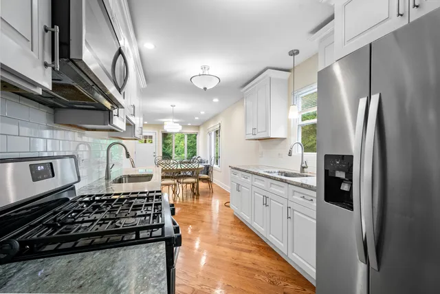 a kitchen with stainless steel appliances granite countertop a stove a refrigerator a sink dishwasher and white cabinets next to a window