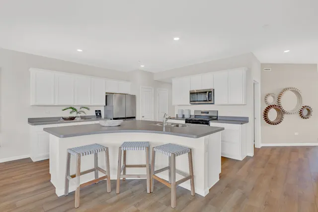 a kitchen with stainless steel appliances granite countertop a sink a stove a refrigerator with white cabinets and wooden floor