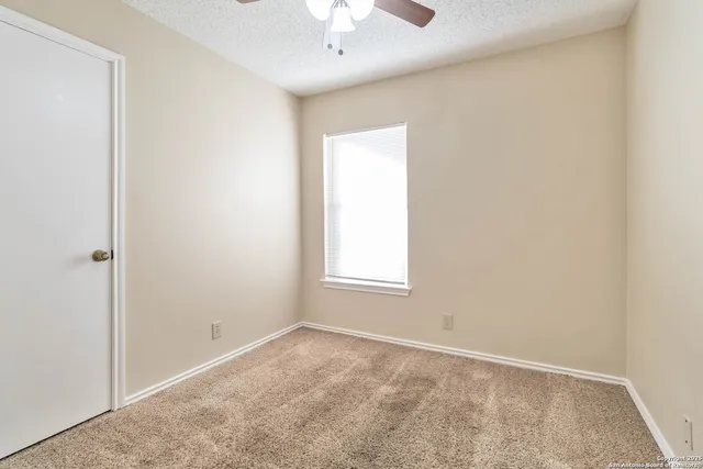 an empty room with a chandelier fan and windows