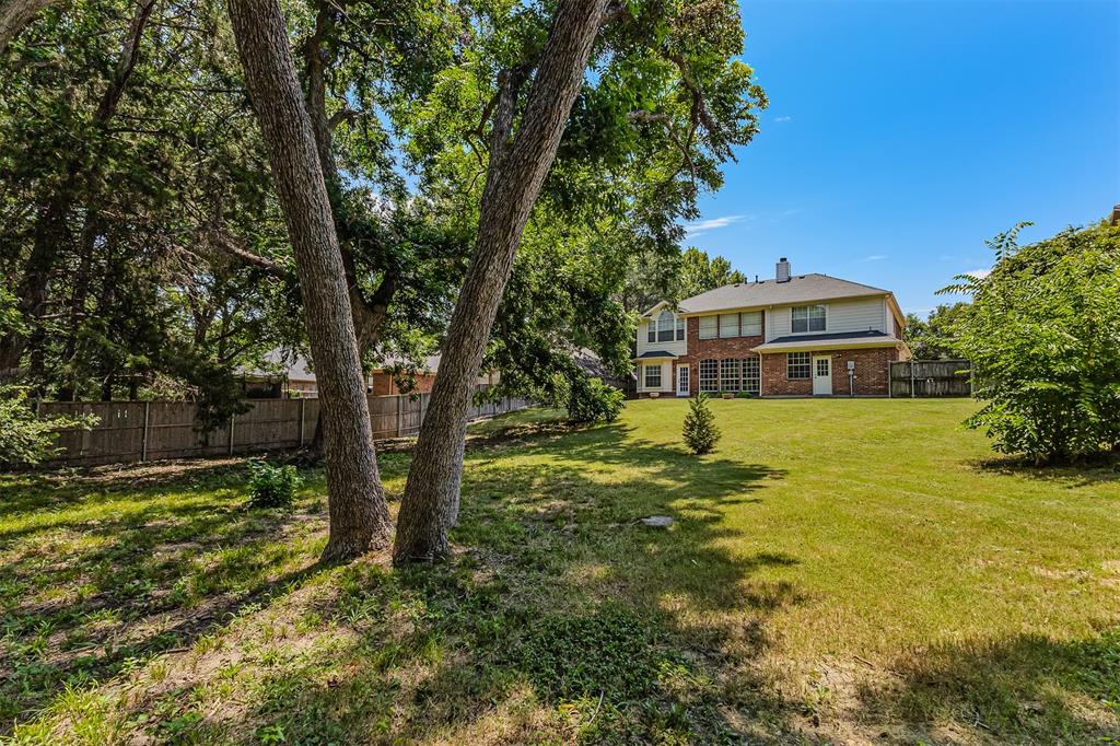 9301 Nottingham Court Rowlett, TX 75088 - Photo 35 of 39 Expansive backyard featuring a manicured lawn, established trees, and a two-story residence with a brick and siding exterior