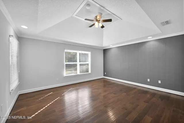 an empty room with wooden floor chandelier fan and windows