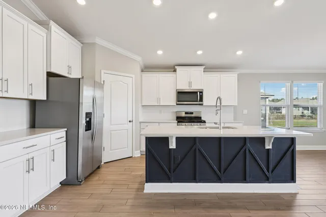 a kitchen with stainless steel appliances a sink dishwasher a stove and white cabinets with wooden floor