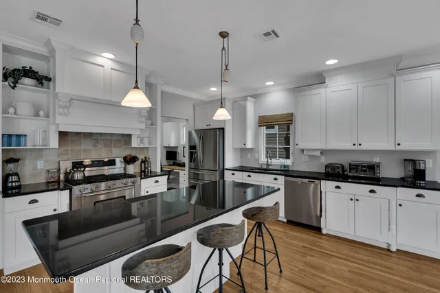 a kitchen with granite countertop a stove a sink a refrigerator and chairs