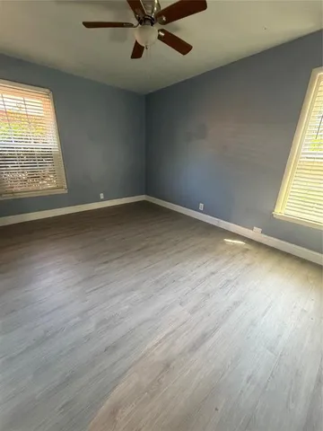an empty room with wooden floor fan and windows