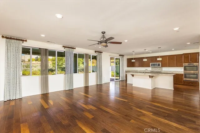a view of an empty room with kitchen view and a large window with wooden floor
