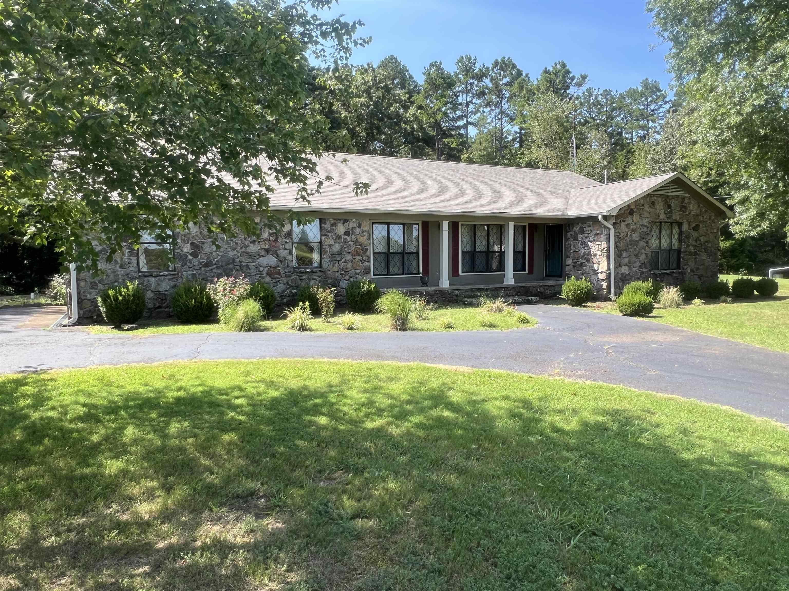 1250 Clifft Road Bolivar, TN 38008 - Photo 2 of 13 Stone veneer exterior with a covered porch, established landscaping, a paved driveway, and mature trees