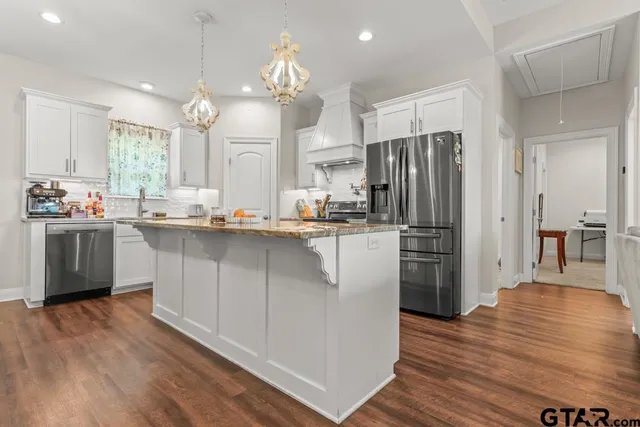 a kitchen with stainless steel appliances a refrigerator a sink dishwasher a stove and white cabinets with wooden floor