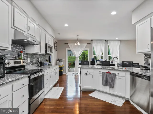 a kitchen with stainless steel appliances granite countertop a stove top oven a sink dishwasher and white cabinets with wooden floor
