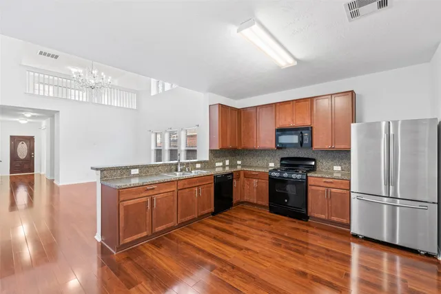 a kitchen with stainless steel appliances granite countertop a refrigerator a sink dishwasher a stove with wooden cabinets and floor