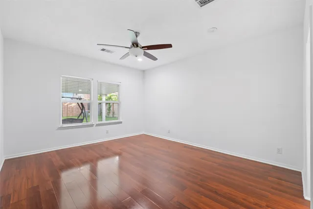 an empty room with wooden floor fan and windows