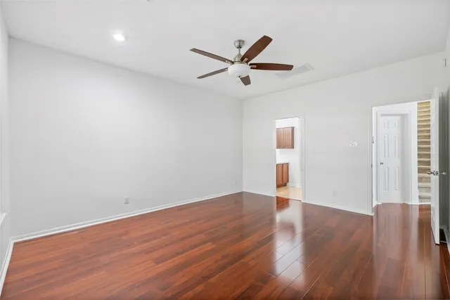a view of an empty room with wooden floor and a ceiling fan