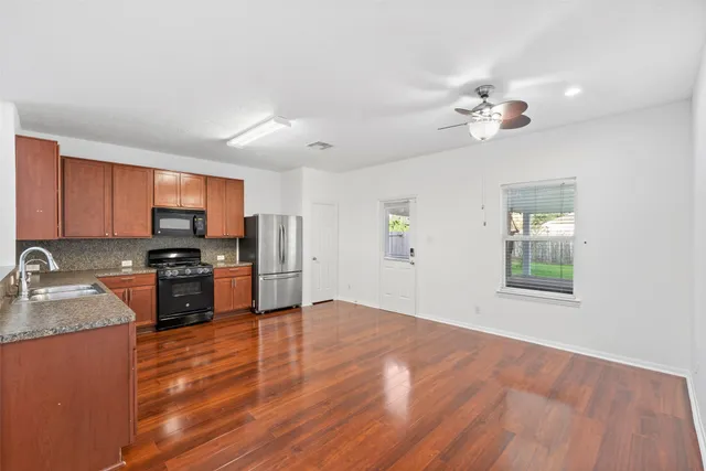 a open kitchen with stainless steel appliances granite countertop a stove top oven a sink dishwasher a dining table and chairs with wooden floor