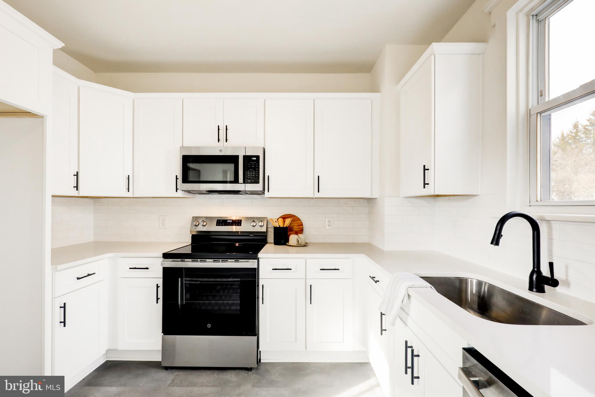 7301 North Radcliffe Street Bristol, PA 19007 - Photo 14 of 43 a kitchen with white cabinets a sink and a stove with wooden floor