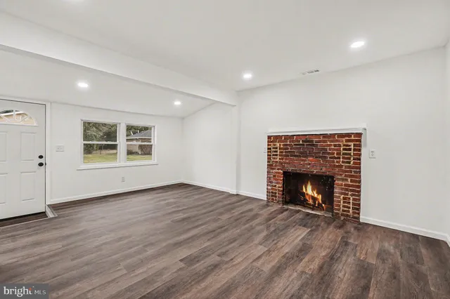 an empty room with wooden floor fireplace and windows