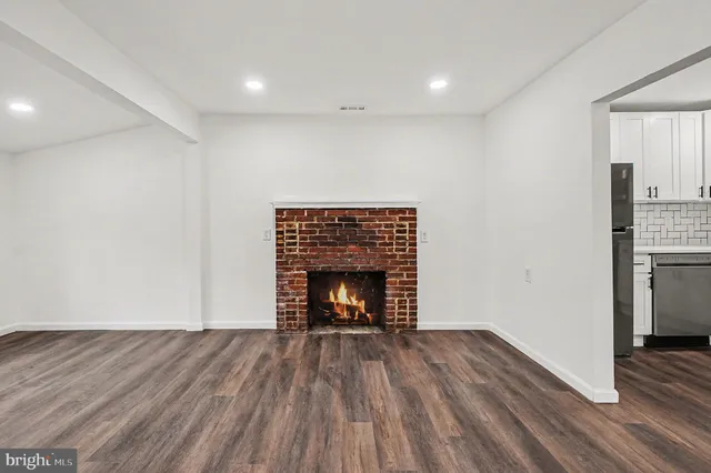 a view of an empty room with wooden floor fireplace and a window