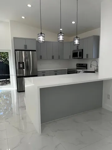 a large white kitchen with a large island oven a stove a sink a refrigerator and a fireplace