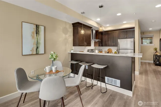 a room with stainless steel appliances kitchen island granite countertop a dining table chairs and a refrigerator