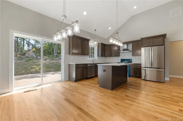 a kitchen with stainless steel appliances a stove top oven a sink dishwasher a refrigerator with white cabinets and wooden floor