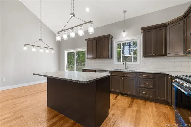 a kitchen with stainless steel appliances granite countertop wooden cabinets a sink dishwasher a stove and a refrigerator with wooden floor