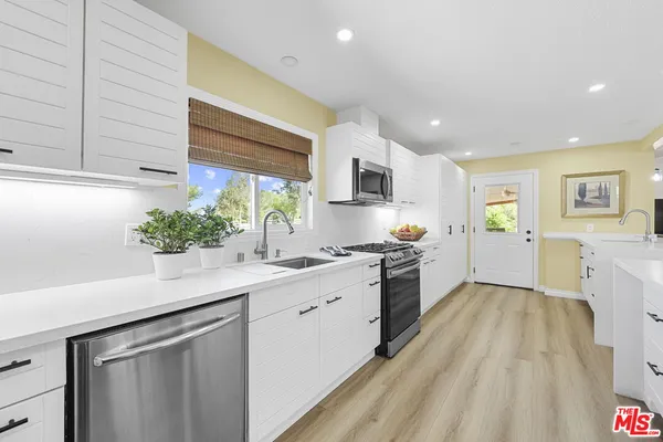 a kitchen with a sink dishwasher stove and white cabinets with wooden floor